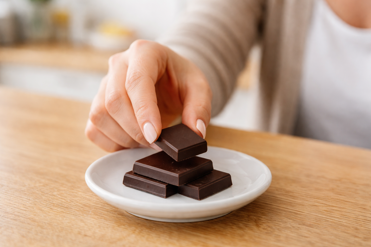 Ręka sięga po jedną kostkę czekolady z talerza